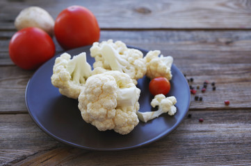Fresh cauliflower and cherry tomatoes on a brown round plate on a wooden surface close up, soft focus