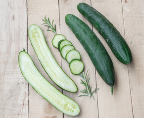 Fresh and ripped cucumbers decorated with rosemary on wooden des