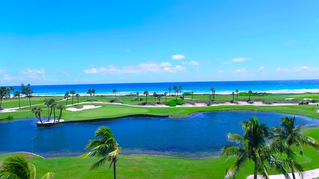 Aerial - Beautiful view of Golf Course next to ocean going up next to palm trees 