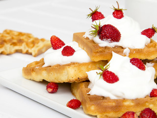 waffles with wild strawberries and whipped cream on white table