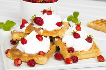waffles with wild strawberries and whipped cream on white table