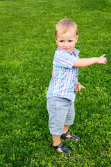 Adorable little smiling boy standing at the lawn at grass