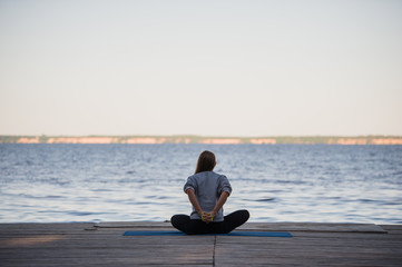 Fototapeta premium Woman doing stretching yoga exercises in the morning at the pier near sea or lake