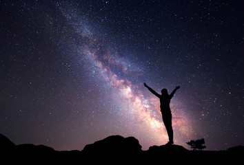 Milky Way. Night sky with stars and silhouette of a woman with raised-up arms.