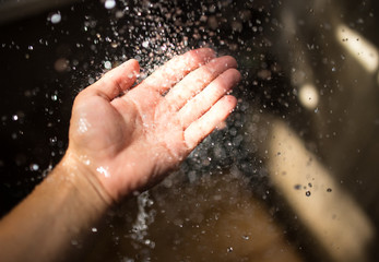 Fototapeta na wymiar Human hand in sunlight under falling water.