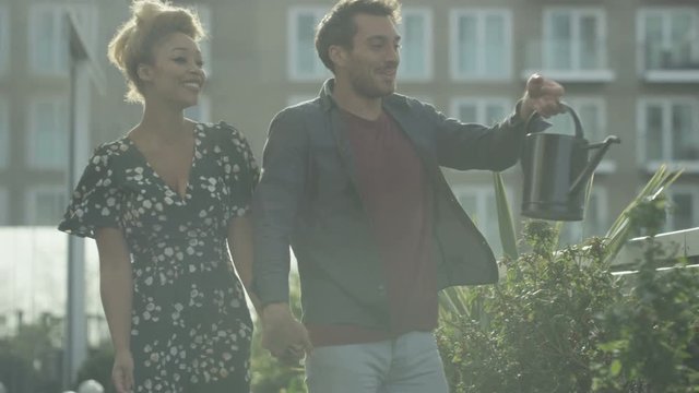  Young Romantic Couple Water Plants & Look Out At View In Apartment Garden