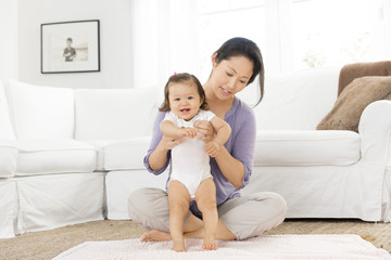 Mother helping baby girl stand in living room