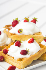 waffles with wild strawberries and whipped cream on white table