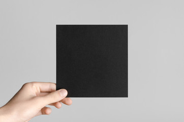 Black Square Flyer / Invitation Mock-Up - Male hands holding a black flyer on a gray background.