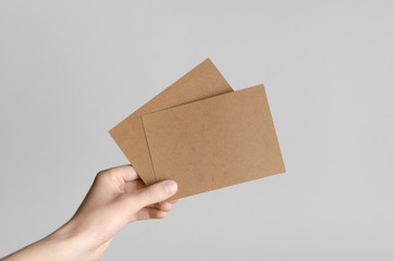 Kraft A6 Flyer / Postcard / Invitation Mock-Up - Male hands holding blank flyers on a gray background.