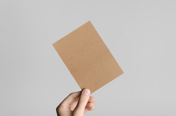 Kraft A6 Flyer / Postcard / Invitation Mock-Up - Male hands holding a blank flyer on a gray background.