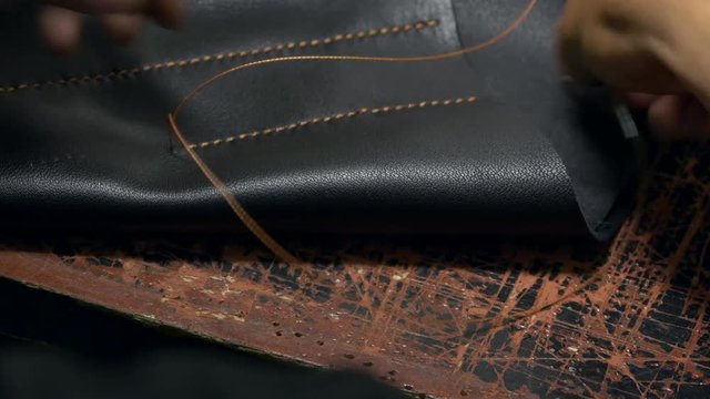 Furrier works with synthetic leather fabric. Master skin and leather pierces the leatherette by large needle with nylon thread. Handcrafted and handmade  professional accessory. Back view. Close shot