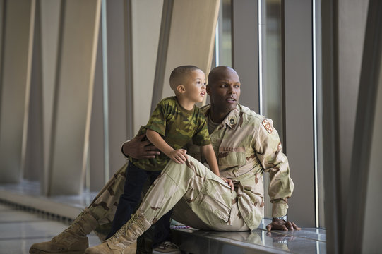 African American soldier and son looking out airport window
