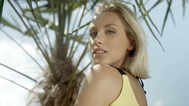 Sexy blonde girl posing on tropical beach. Young beautiful blonde girl under tropical palm trees. Fashion portrait of pretty young hipster girl with short hair.