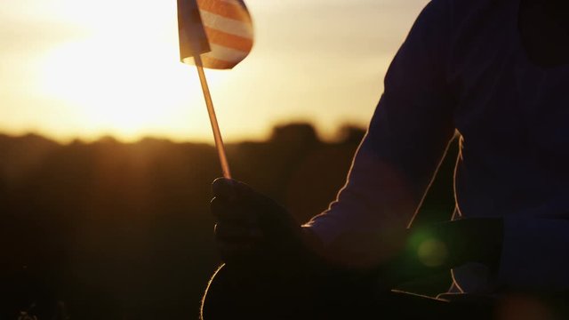  Silhouette of a young child holding a US flag at sunset, in slow motion