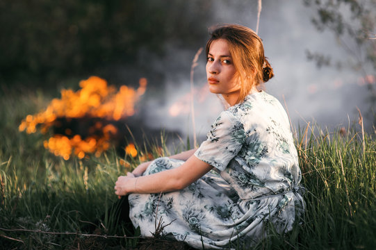 Portrait Of Woman Sitting Near Fire In Field