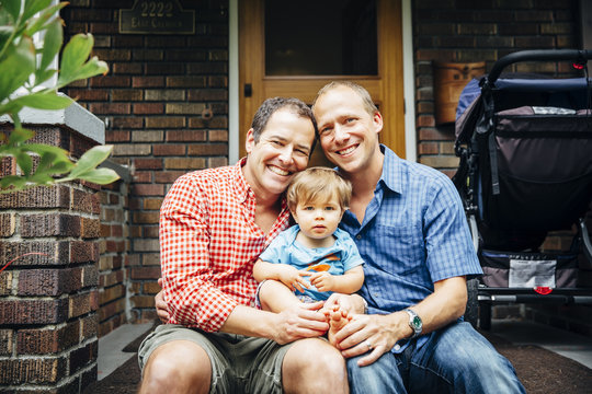 Gay fathers holding baby son on front stoop