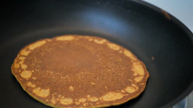 Close up slow motion shot of a spatula flipping a pancake in a skillet.
