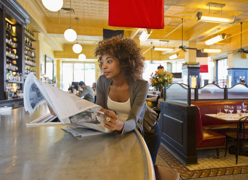 African American woman reading newspaper in cafe