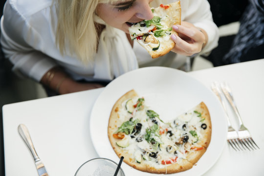 Caucasian woman eating slice of pizza in restaurant