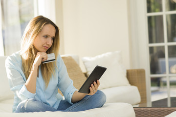 Woman holding credit card while shopping online using digital tablet