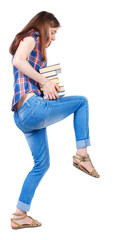 Girl carries a heavy pile of books. back view.  Rear view people collection.  backside view of person.  Isolated over white background. Girl in plaid shirt supports the knee pile of books