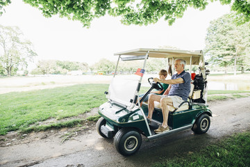 Grandfather and grandson in golf cart on golf course