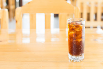 Cola soda with ice in glass on wooden table