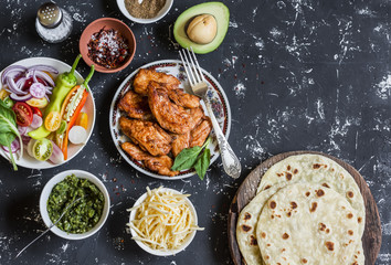 Spicy grilled chicken, tortilla, avocado, cheese, vegetables on a dark background, top view