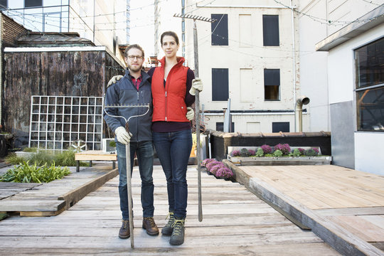 Couple holding rakes in urban rooftop garden