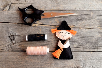 Halloween felt witch with broom, beige and black thread, needle, scissors on old wooden background....