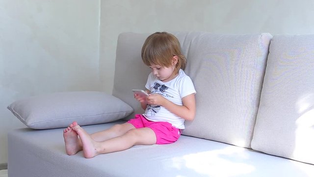 Little girl plays on phone and smille looks to camera