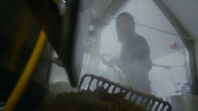  Worker in a brewery removing mash from the bottom of a machine