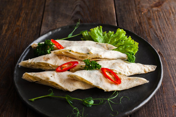 Homemade rolls from lavash with sweet pepper on wooden background. Traditional caucasian snack, served on black plate, rustic style