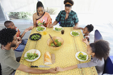 Black family saying grace at dining room table