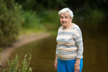 An elderly woman stands in the Park near the pond.