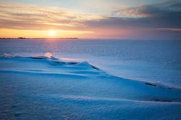 Beautiful winter landscape with frozen lake, crack and sunset sky