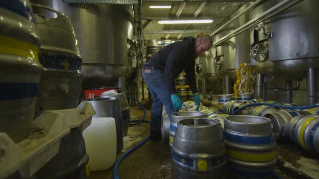  Worker in a brewery filling barrels of beer with a hose