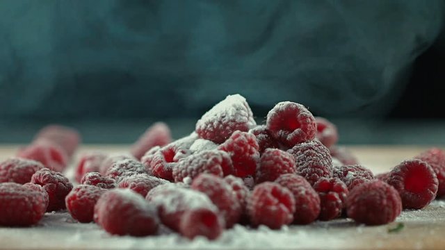 White vapor falling on the heap of red sugar powdered raspberries on the wooden surface