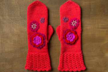 Knitted red mittens with flowers on wooden background