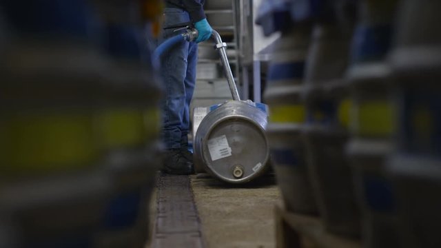  Worker in a brewery filling barrels of beer with a hose. 
