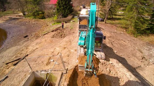 The aerial shot of the land where the backhoe is digging a deep hole and transferring the soil on the big dum truck