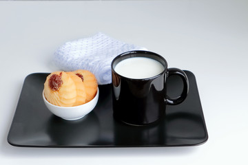 Milk and cookies served on a black plate. White background.