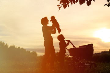 Silhouette of father with two kids walking at sunset, happy family
