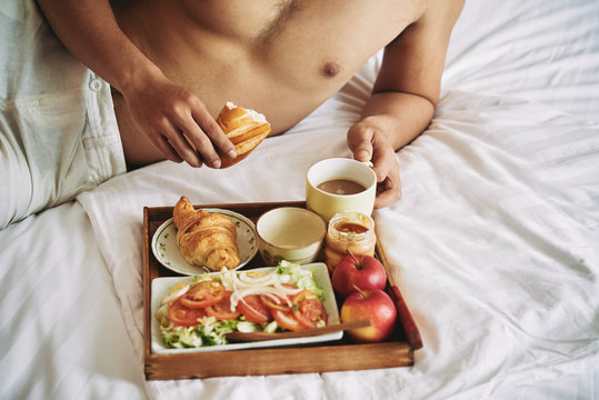 Tray with healthy breakfast on bed of man
