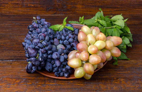 pink and blue grapes in a clay plate on a wooden background