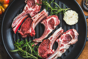 Raw uncooked lamb meat chops with rosemary and garlic in black iron grilling pan, top view,...