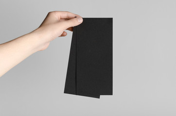 Black DL Flyer Mock-Up - Male hands holding black flyers on a gray background.
