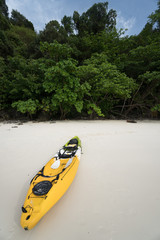 A yellow kayak on a tropical beach over green trees background