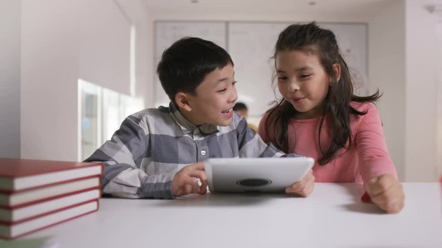 Happy little boy and girl working on computer tablet in school classroom